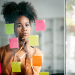 Jovem analisa ideias em mural de post-its coloridos no escritório.