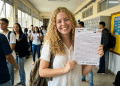 Jovem sorridente exibe folha de redação do Enem em escola.