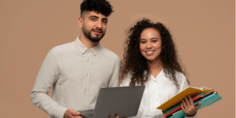 Professores sorridentes com laptop e cadernos sobre fundo bege.