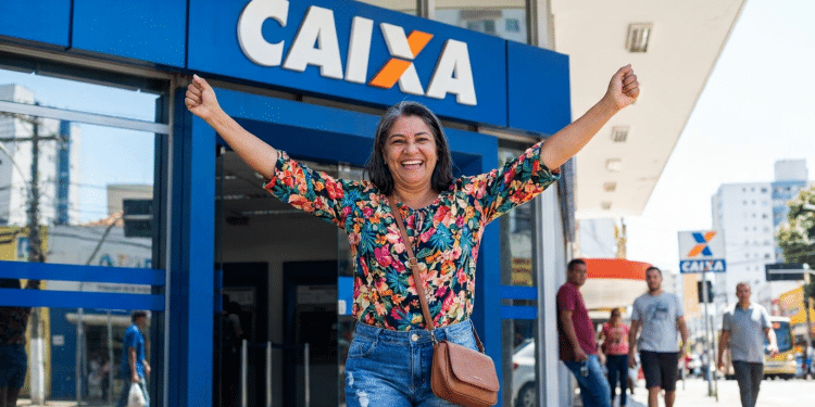 Mulher celebra saque na Caixa Econômica Federal em frente à agência.