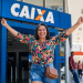 Mulher celebra saque na Caixa Econômica Federal em frente à agência.