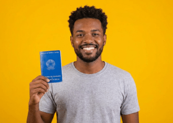 Jovem negro sorrindo exibe Carteira de Trabalho azul.