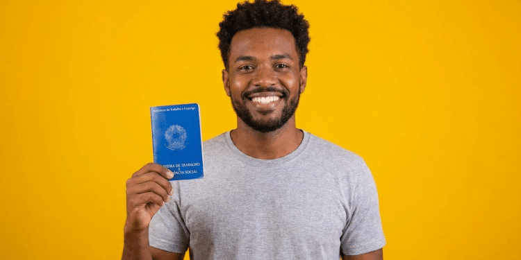 Jovem negro sorrindo exibe Carteira de Trabalho azul.