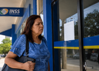 Mulher observa porta fechada de agência do INSS com expressão preocupada na calçada