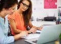 Duas profissionais analisam dados no escritório, representando os cursos que aceleram a entrada no mercado de trabalho