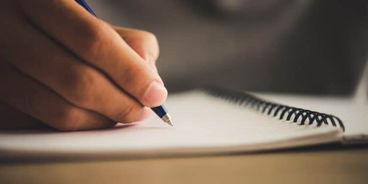 Mão escreve em caderno espiral, representando as profissões para quem gosta de escrita e digitação