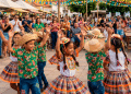 Crianças dançando em festa junina enquanto pessoas assistem ao arraial.