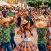 Crianças dançando em festa junina enquanto pessoas assistem ao arraial.