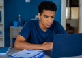 Estudante jovem utilizando notebook e materiais de estudo em casa durante preparação para o Enem.