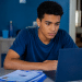Estudante jovem utilizando notebook e materiais de estudo em casa durante preparação para o Enem.