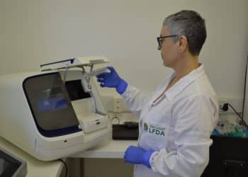 Perita de jaleco opera equipamento em laboratório, retratando o trabalho do Fiscal Federal Agropecuário