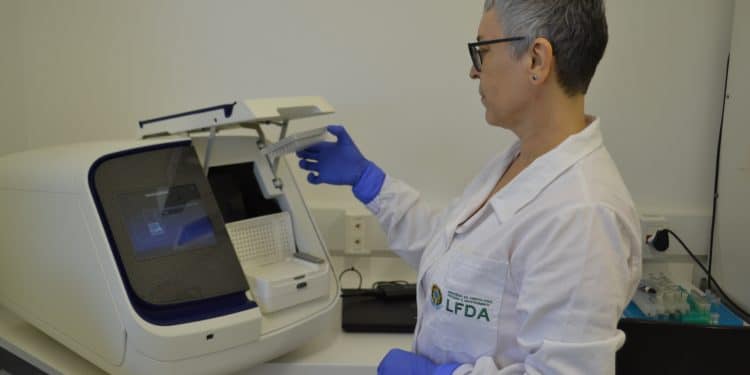 Perita de jaleco opera equipamento em laboratório, retratando o trabalho do Fiscal Federal Agropecuário
