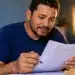 Homem analisando documentos em casa, com muletas ao fundo, representando o processo de solicitação do auxílio-acidente do INSS.