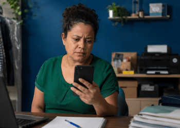 Microempreendedora consultando benefícios do INSS pelo celular em pequeno ambiente de trabalho.