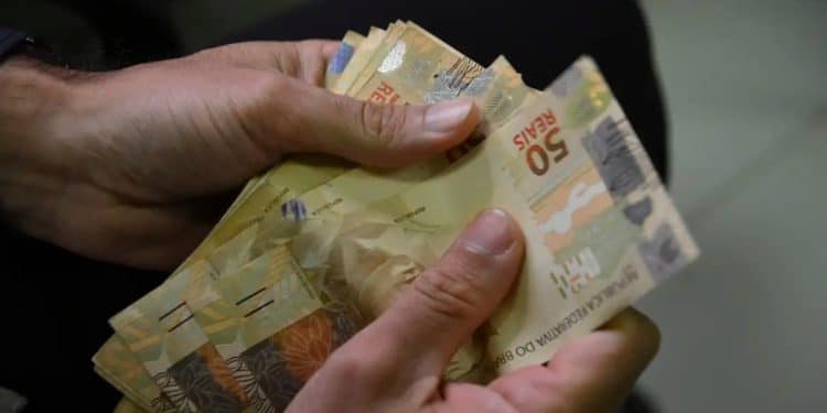 Pessoa conta cédulas de R$ 50, representando a soma do Bolsa Família com o Incentivo-Conclusão do Pé-de-Meia