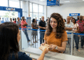 Mulher recebe cédulas no caixa de uma agência da Caixa com fila ao fundo