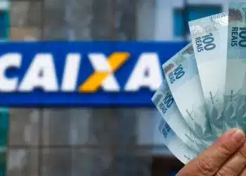 Cédulas de R$ 100 em frente a uma agência da Caixa Econômica Federal ilustram o pagamento de R$ 1.050 do Bolsa Família.
