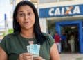 Beneficiária com o dinheiro do Bolsa Família em frente a uma agência da Caixa, banco que pode antecipar o pagamento de junho para o sábado