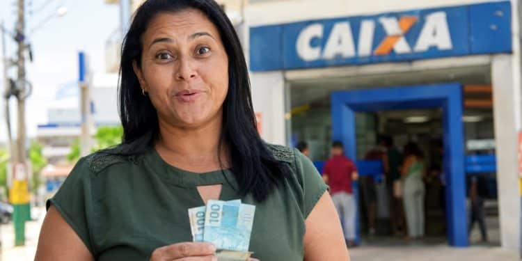 Beneficiária com o dinheiro do Bolsa Família em frente a uma agência da Caixa, banco que pode antecipar o pagamento de junho para o sábado