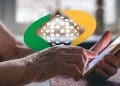 Idosa consulta a data de pagamento do BPC pelo celular, com a marca do INSS ao fundo