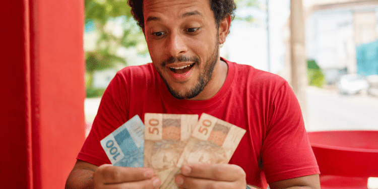 Homem sorri surpreso ao contar notas de cem e cinquenta reais em ambiente externo