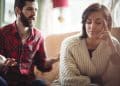 Mulher pensativa e cabisbaixa ao lado de homem que fala gesticulando no sofá, representando jogos mentais em uma conversa