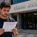 Jovem lê documento de concurso público em frente à Câmara Municipal, representando inscrições abertas para cargo com salário de R$ 15,6 mil.