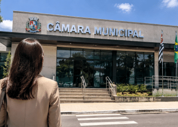 Pessoa em frente à Câmara Municipal representando divulgação de concurso público com vagas para níveis fundamental e médio.