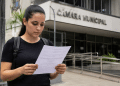 Candidata lê documento de concurso em frente à Câmara Municipal antes do fim das inscrições.