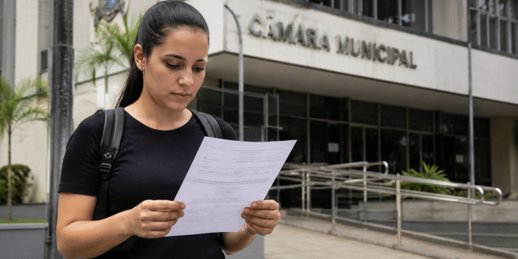 Candidata lê documento de concurso em frente à Câmara Municipal antes do fim das inscrições.