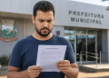 Homem lendo edital de concurso público em frente à Prefeitura Municipal.