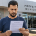 Homem lendo edital de concurso público em frente à Prefeitura Municipal.