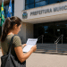 Candidata lê documento de concurso público em frente à Prefeitura Municipal.