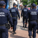 Guardas municipais fardados caminham em patrulhamento na rua.