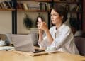 Mulher trabalha em home office com notebook sobre a mesa enquanto utiliza o celular como apoio à conexão de internet