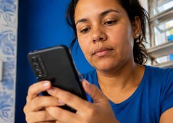 Mulher de camiseta azul consulta atenta a tela do celular para verificar a restrição de um aparelho pelo IMEI.