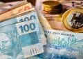 Cédulas de R$ 50 e R$ 100 e moeda de R$ 1 sobre notas do Banco Central, representando o dinheiro esquecido que pode ser resgatado no Sistema de Valores a Receber.