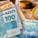 Cédulas de R$ 50 e R$ 100 e moeda de R$ 1 sobre notas do Banco Central, representando o dinheiro esquecido que pode ser resgatado no Sistema de Valores a Receber.
