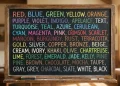 Quadro escolar com nomes de cores em inglês escritos em letras coloridas, representando o estudo de vocabulário.