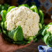 Mão segura couve-flor fresca com folhas verdes em bancada de cozinha