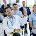 Profissionais de saúde de jaleco assistem a uma palestra, um deles com o braço levantado para participar