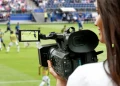 Cinegrafista em estádio de futebol registrando partida ao vivo, destacando atuação profissional no setor esportivo.