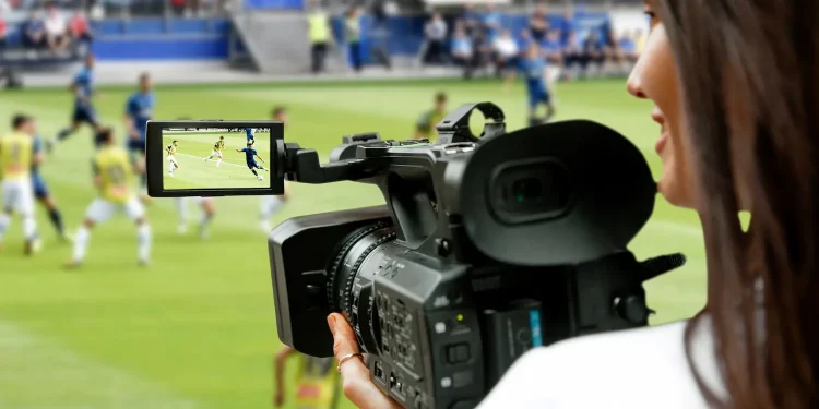 Cinegrafista em estádio de futebol registrando partida ao vivo, destacando atuação profissional no setor esportivo.