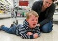 Criança chorando no supermercado com mãe tentando acalmá-la.