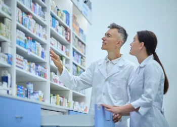 Farmacêuticos observam prateleiras de medicamentos, em imagem relacionada à importância da especialização para alcançar melhores cargos na carreira.
