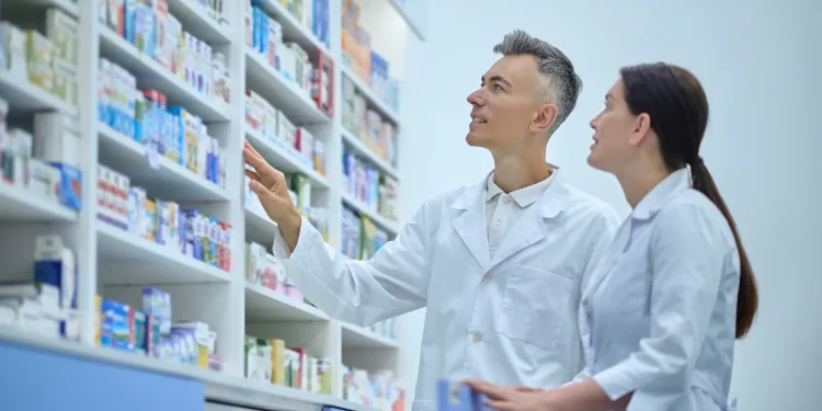 Farmacêuticos observam prateleiras de medicamentos, em imagem relacionada à importância da especialização para alcançar melhores cargos na carreira.
