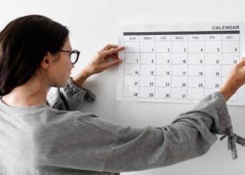 Mulher de óculos observa um calendário de parede para planejar os feriados prolongados de 2026