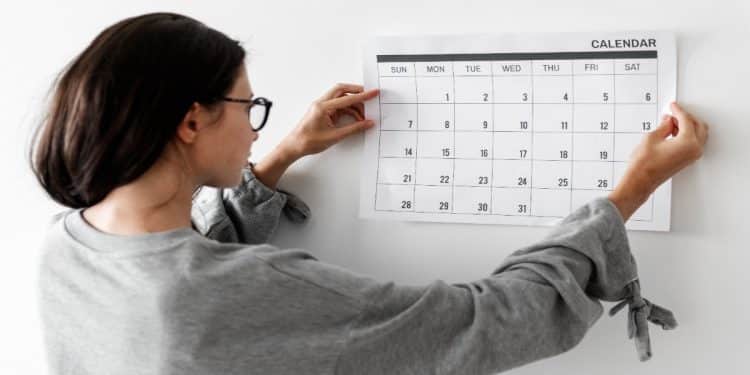Mulher de óculos observa um calendário de parede para planejar os feriados prolongados de 2026
