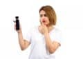 Mulher de camiseta branca observa frasco de perfume preto com expressão de dúvida