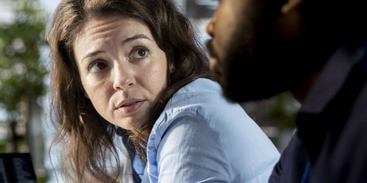 Mulher de cabelo castanho olha séria para colega masculino em escritório iluminado, simbolizando as frases que pessoas mal-educadas dizem.